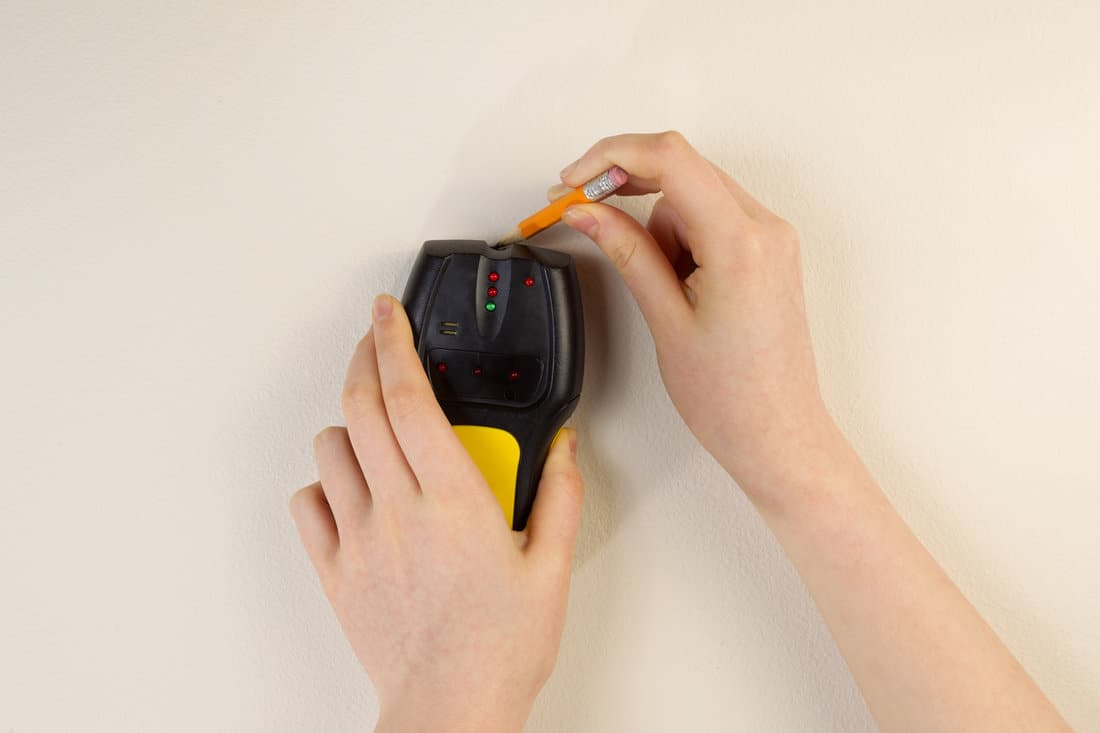 Photo of female hands holding using stud finder and pencil against interior home white wall