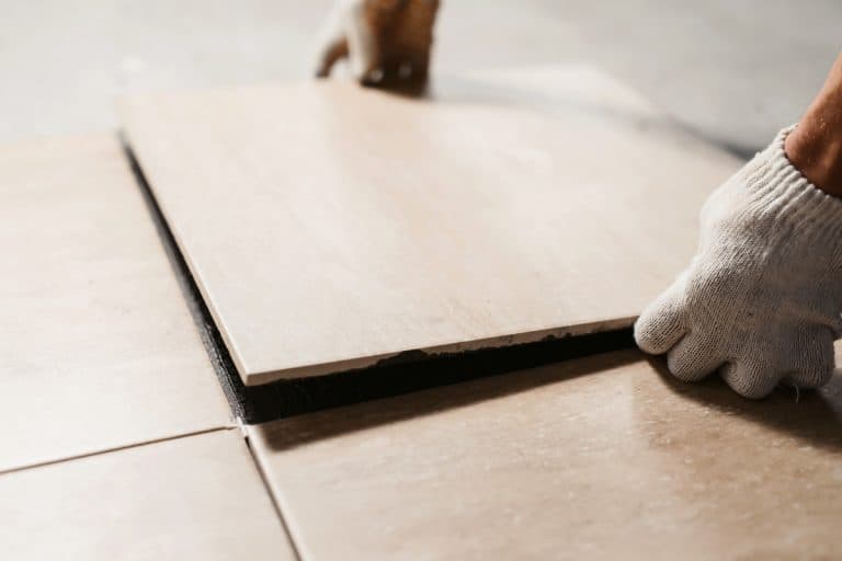 Placing brown ceramic tiles in the for the living room floor, Telltale Signs Of A Bad Tile Job [And How To Fix It]