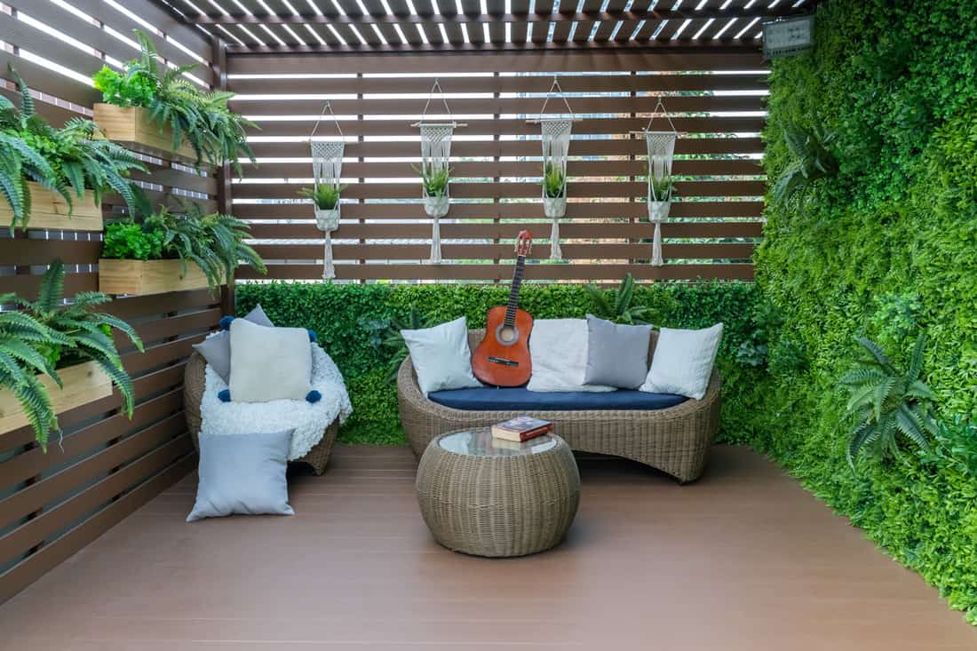 Rattan chairs inside an enclosed balcony with lots of plants and wooden flooring