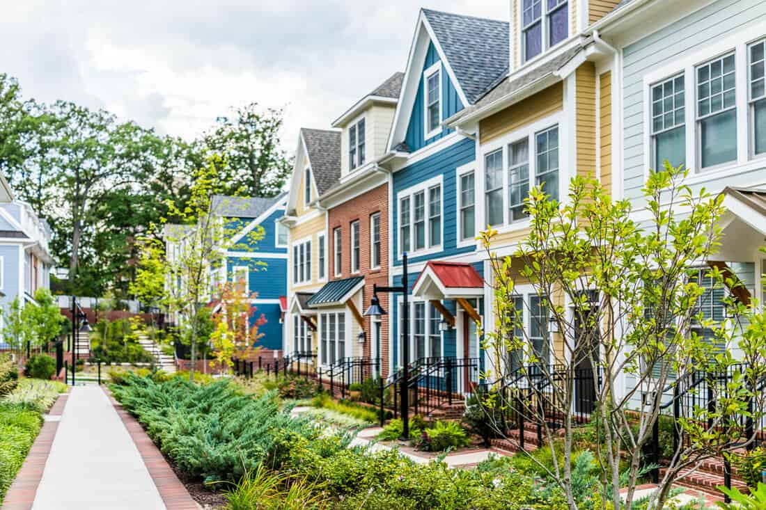 Row of colorful, red, yellow, blue, white, green painted residential townhouses, homes, houses with brick patio gardens in summe