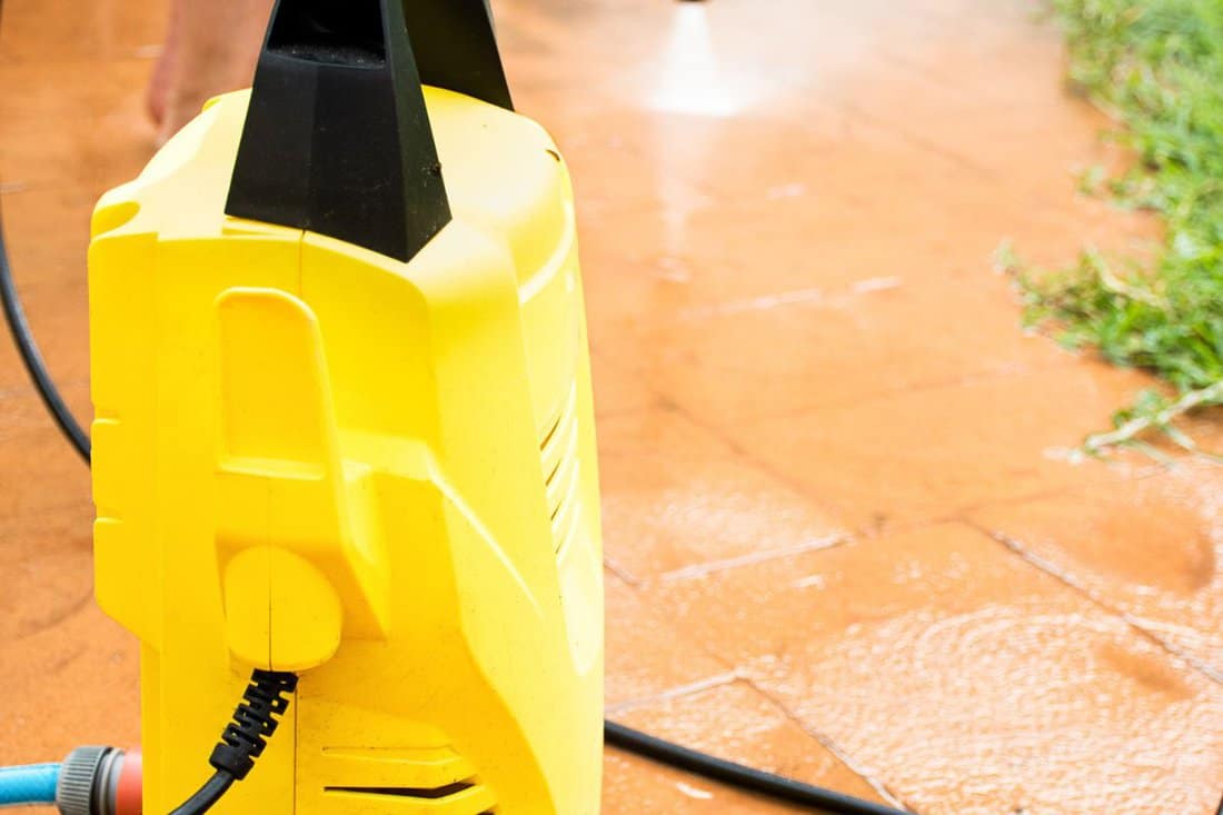 Selective focus. Cleaning backyard paving tiles with high pressure washer. Spring clean up