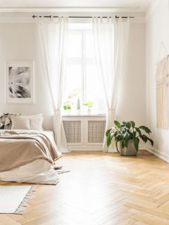 Spacious and bright bedroom interior with beige decorations, hardwood floor and a book on the window sill seat. - Are Sheer Blinds See-Through? [Considerations For Home Decor, Privacy, And Light]