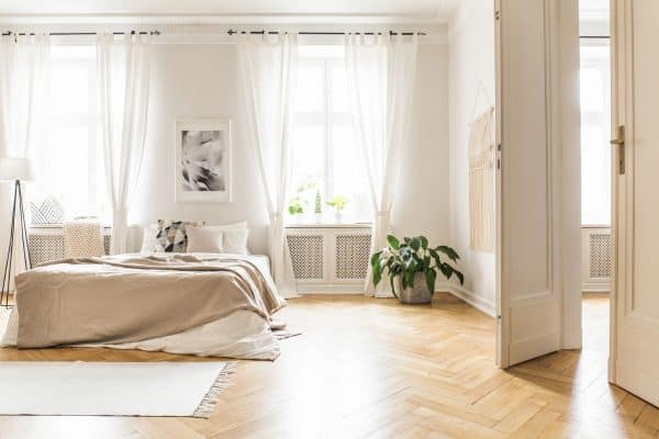 Spacious and bright bedroom interior with beige decorations, hardwood floor and a book on the window sill seat. - Are Sheer Blinds See-Through? [Considerations For Home Decor, Privacy, And Light]