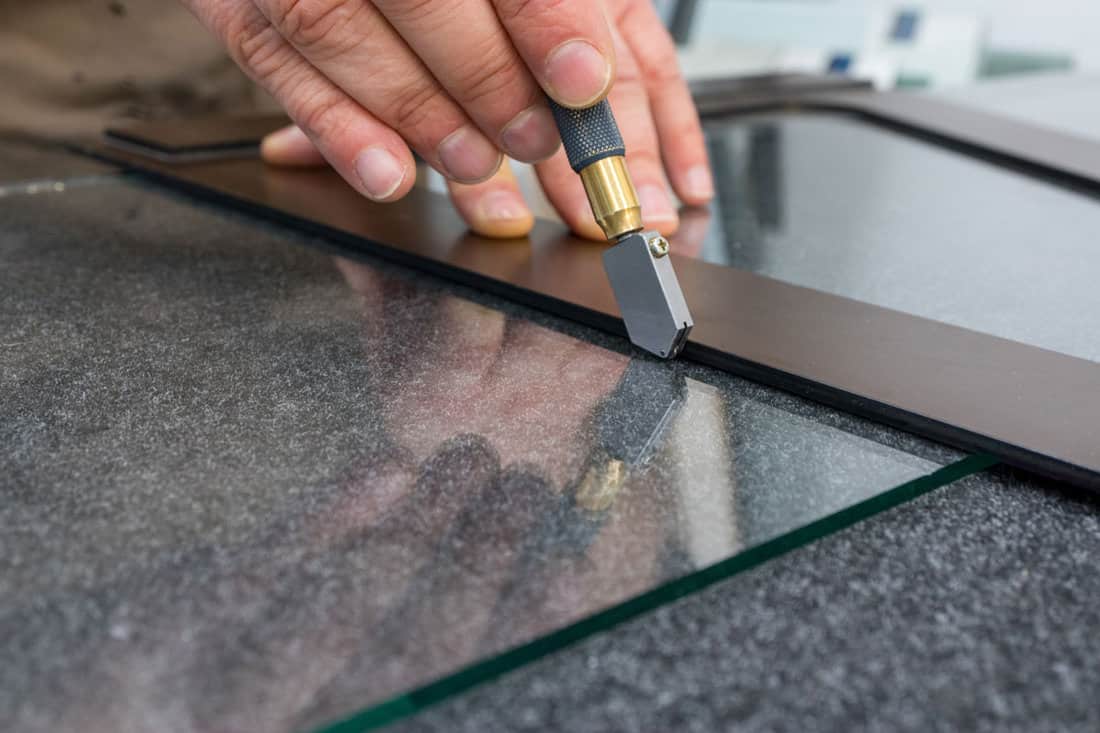The glazier cuts the glass with a hand-held cutting tool