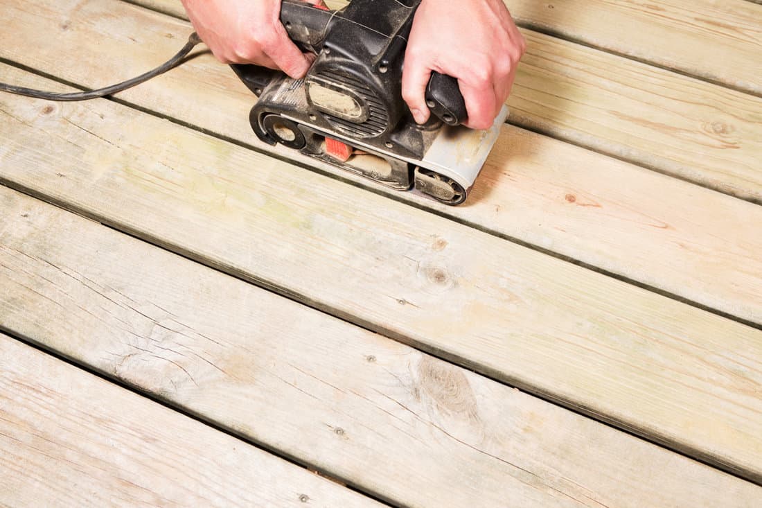 Using a power tool to sand a wooden deck