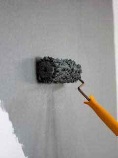 Using a roller paint to paint the wall with a grey color, Telltale Signs Of A Bad Interior Paint Job [& Tips To Repair]