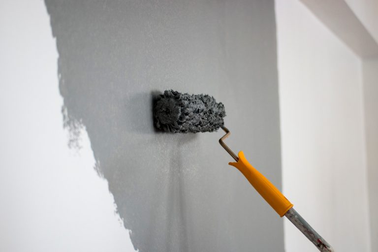 Using a roller paint to paint the wall with a grey color, Telltale Signs Of A Bad Interior Paint Job [& Tips To Repair]