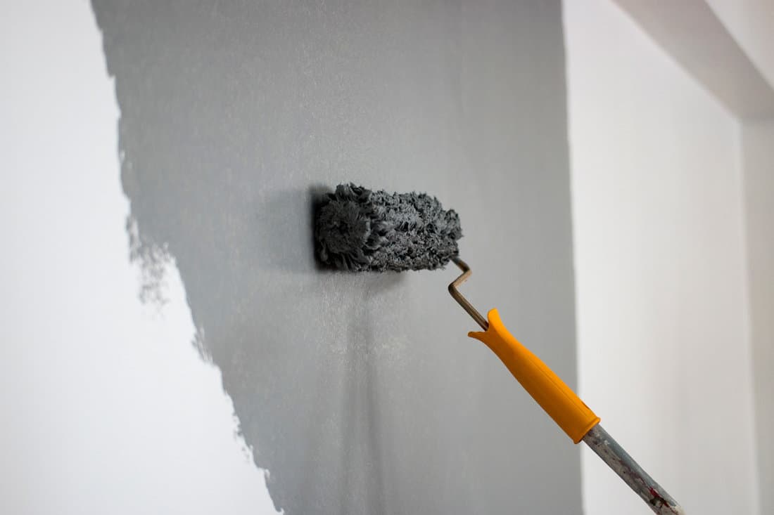Using a roller paint to paint the wall with a grey color