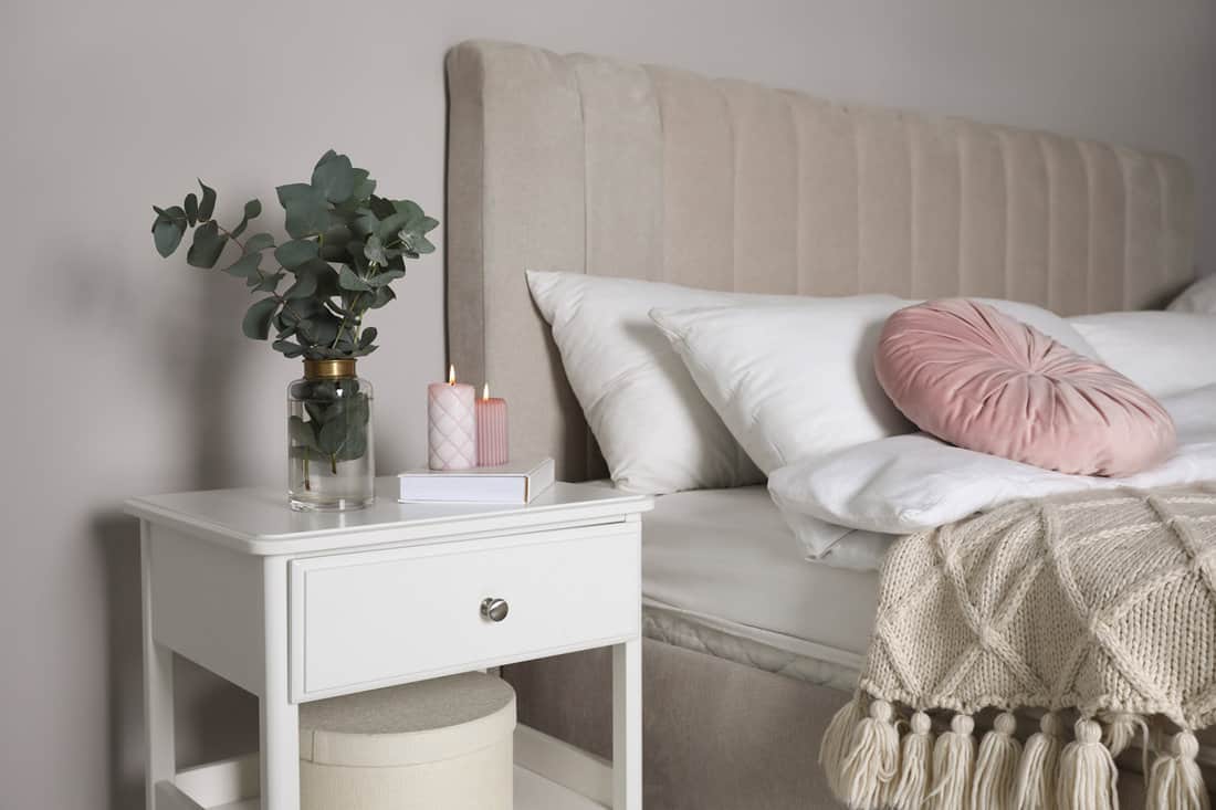 White bedside table with scented candles and a rose