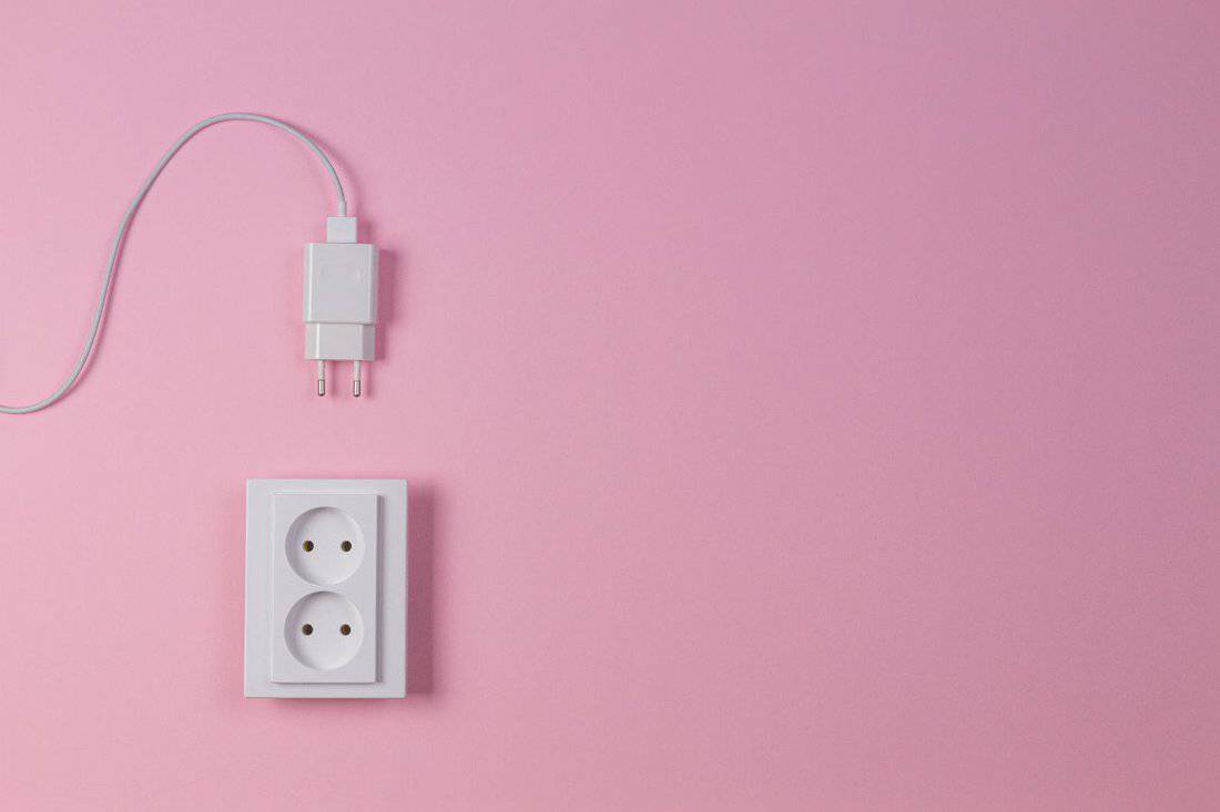 White electrical power socket and power plug on light pink background. Top view.