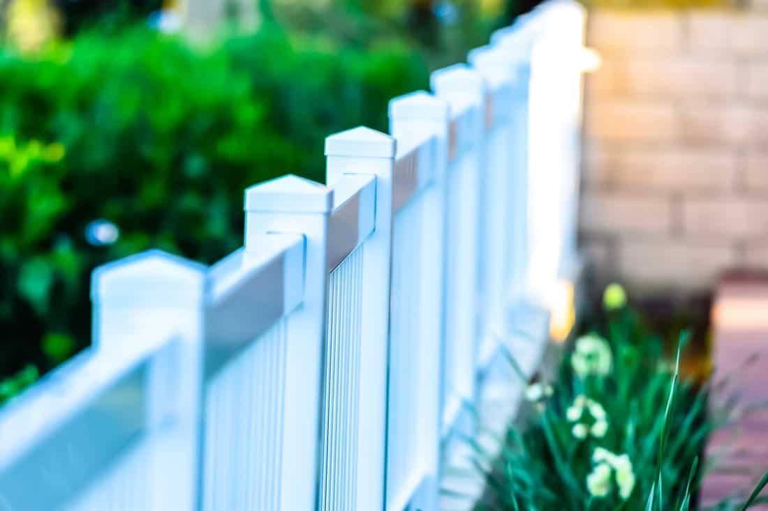 White plastic vinyl picket fence with flowers. Parts in focus while other parts are up of focus.