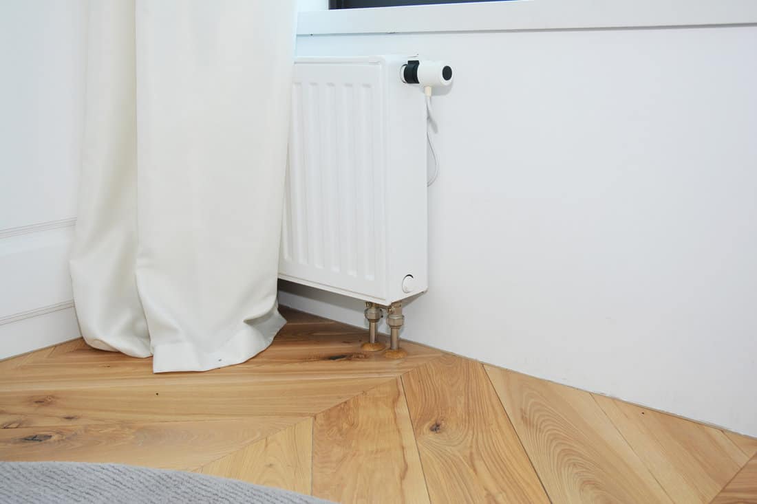 White radiator heating with thermostat for energy saving, wooden floor in the modern room.