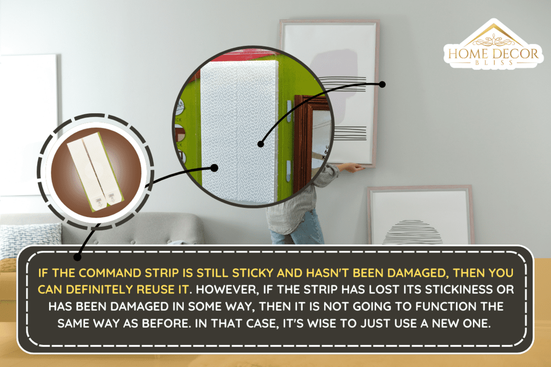 Woman hanging picture on wall in room. Interior design. - Can You Reuse Command Strips?