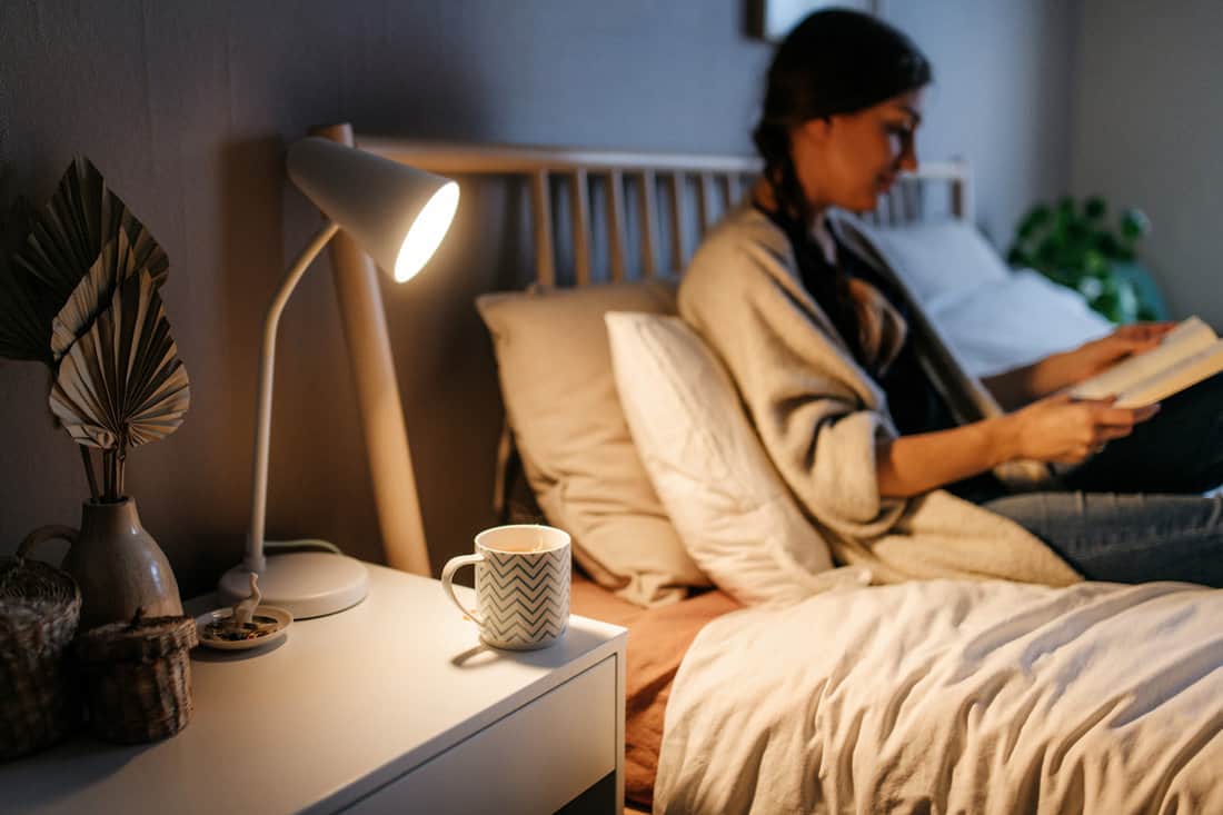 Woman reading her book with tea on the nightstand