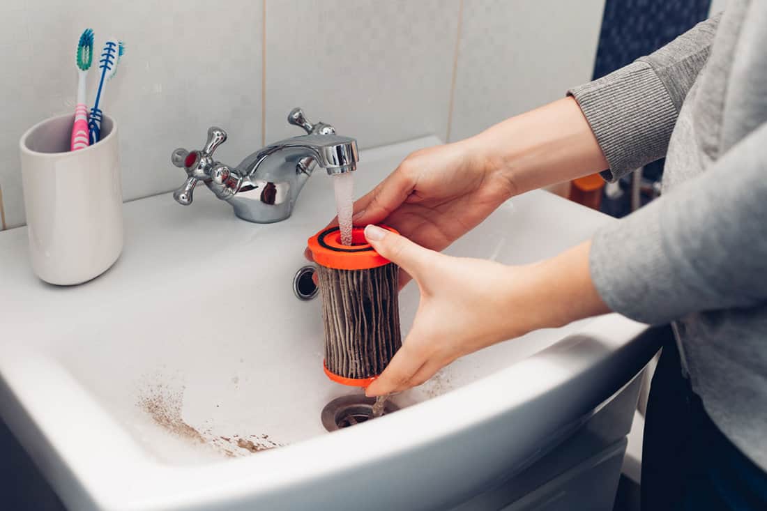 Woman washing dirty filter with water in bathroom sink at home