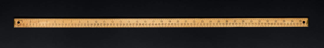 Wooden yardstick on black backgrounds whit centimeters and inches fractions scales.