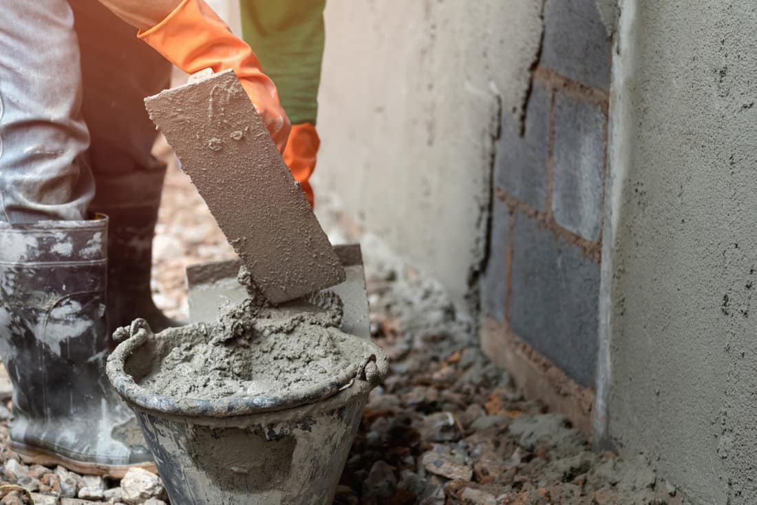 Worker mixing concrete for plastering a wall