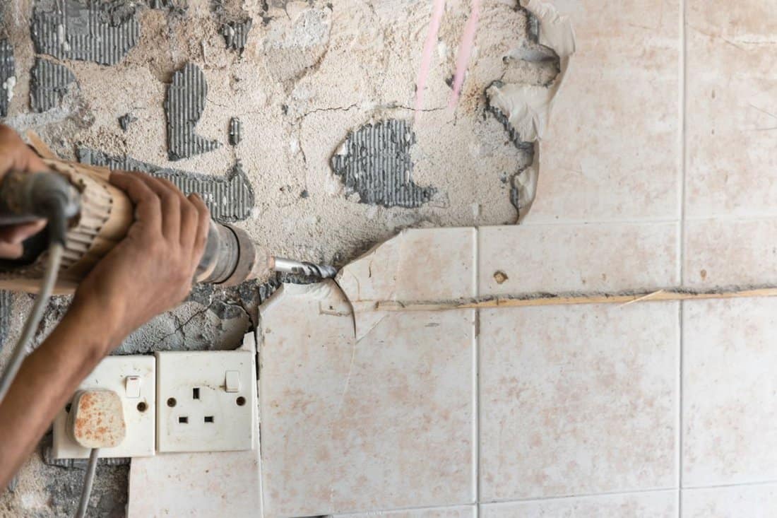 Worker use demolition hammer drill to break up tiles from wall surface in renovation project. Motion blur intended.