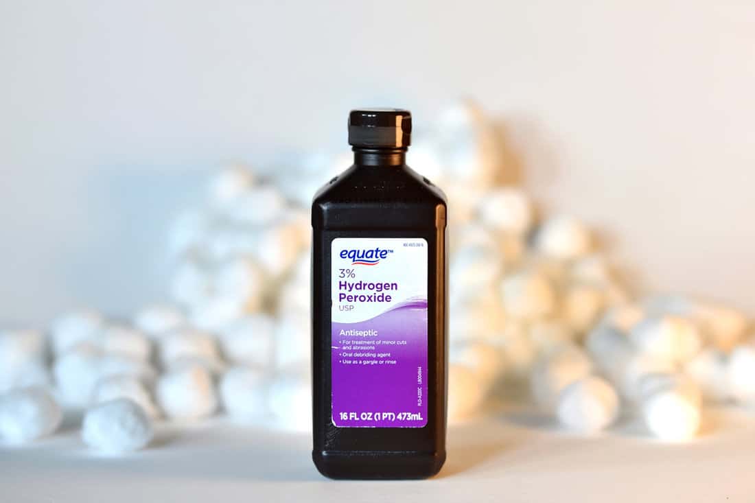  bottle of Equate brand hydrogen peroxide with a pile of cotton balls in the background