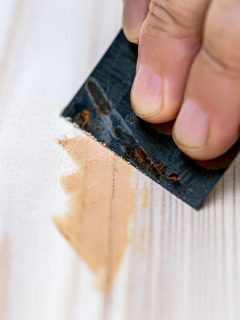 Wood filler brown color with a hand scraping it in the white wood, 5 Best Wood Fillers For Trim [Inc. White Trim]