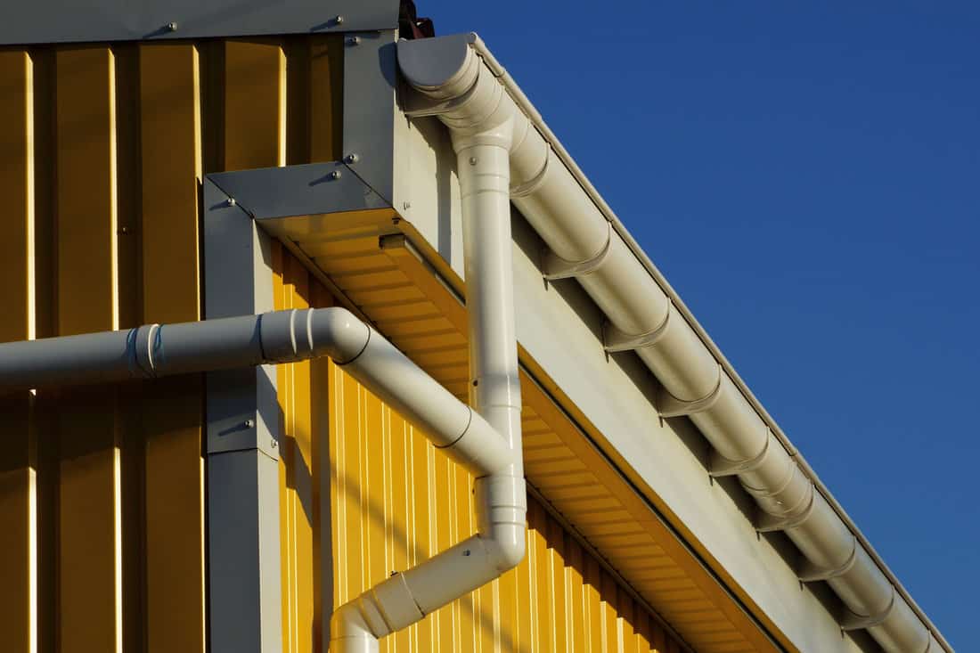 white plastic gutter pipes on the yellow wall of the building on the street against the background of the sky
