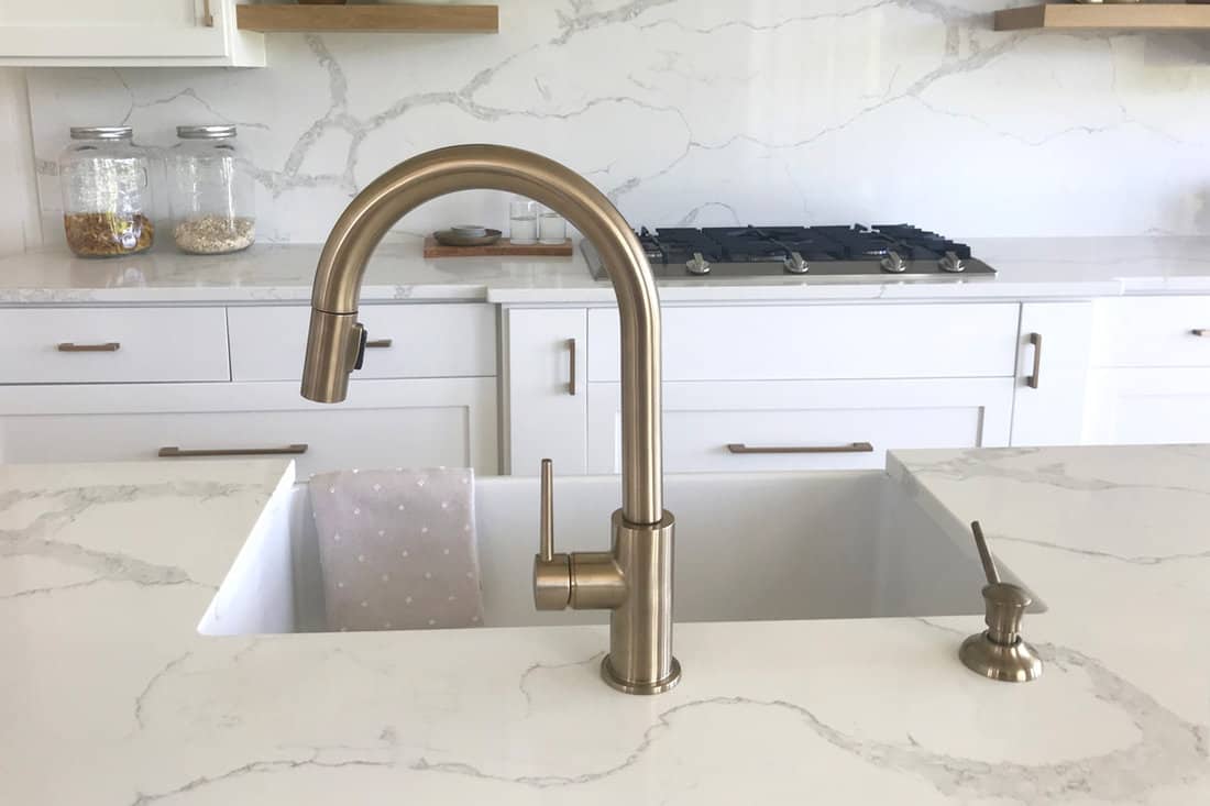 A Moen brass pull down faucet inside luxurious kitchen with Dekton countertop