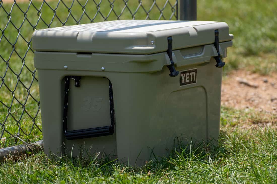 A YETI cooler sits beside a fence, and keeps drinks cold on a hot summer day.