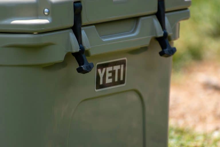 A YETI cooler sits beside a fence, and keeps drinks cold on a hot summer day - How To Remove & Replace Yeti Latches [Step-By-Step Detail]