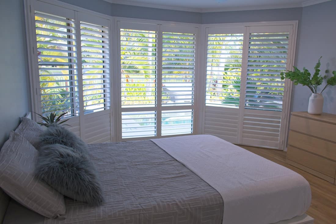 A bay window bedroom with white window shutters