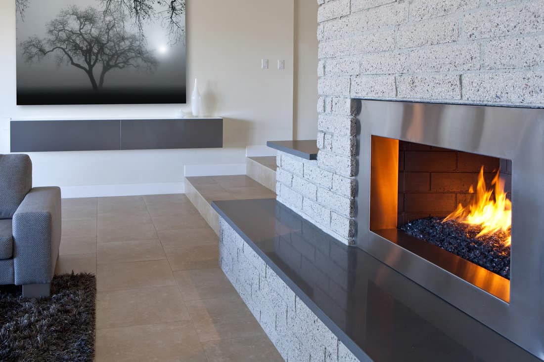 A fireplace in a modern living room with marble flooring a gray furnitures