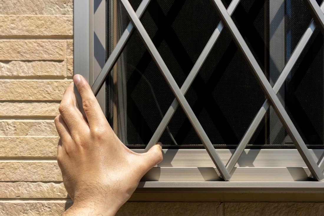 A man's hand checking the grid of a window