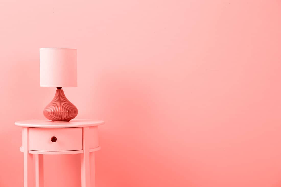 A pink colored end table with a matching pink lamp and coral painted wall