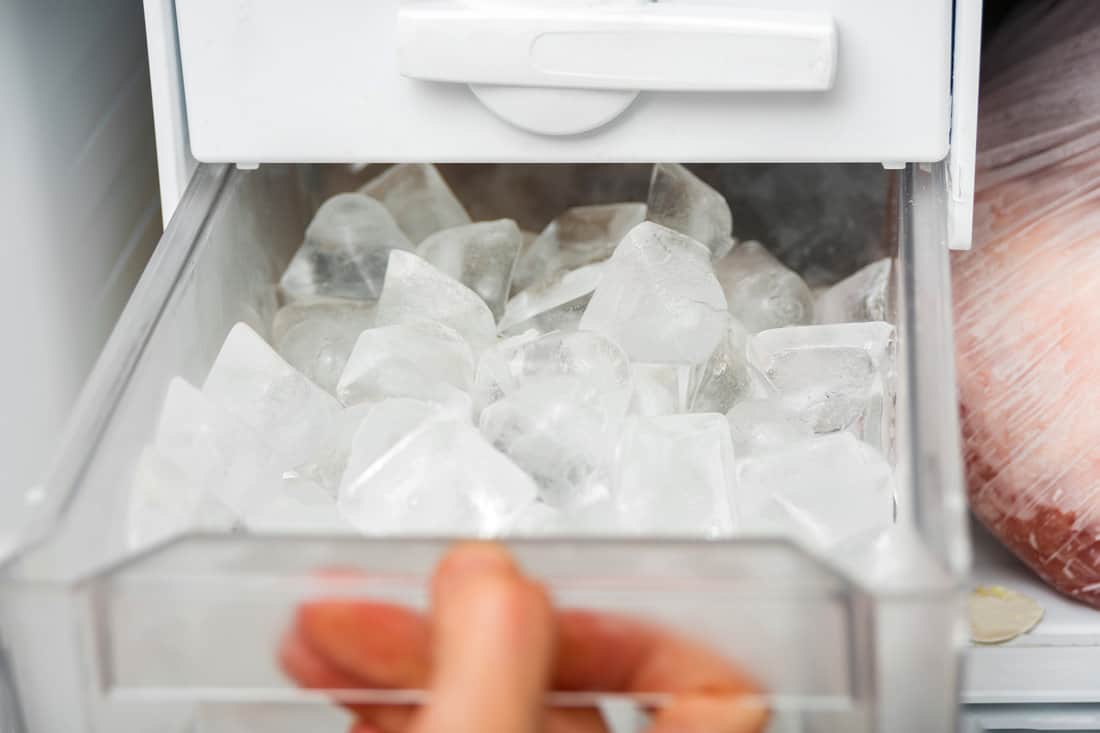 A woman opens an ice maker tray in the freezer to take ice cubes to cool drinks.