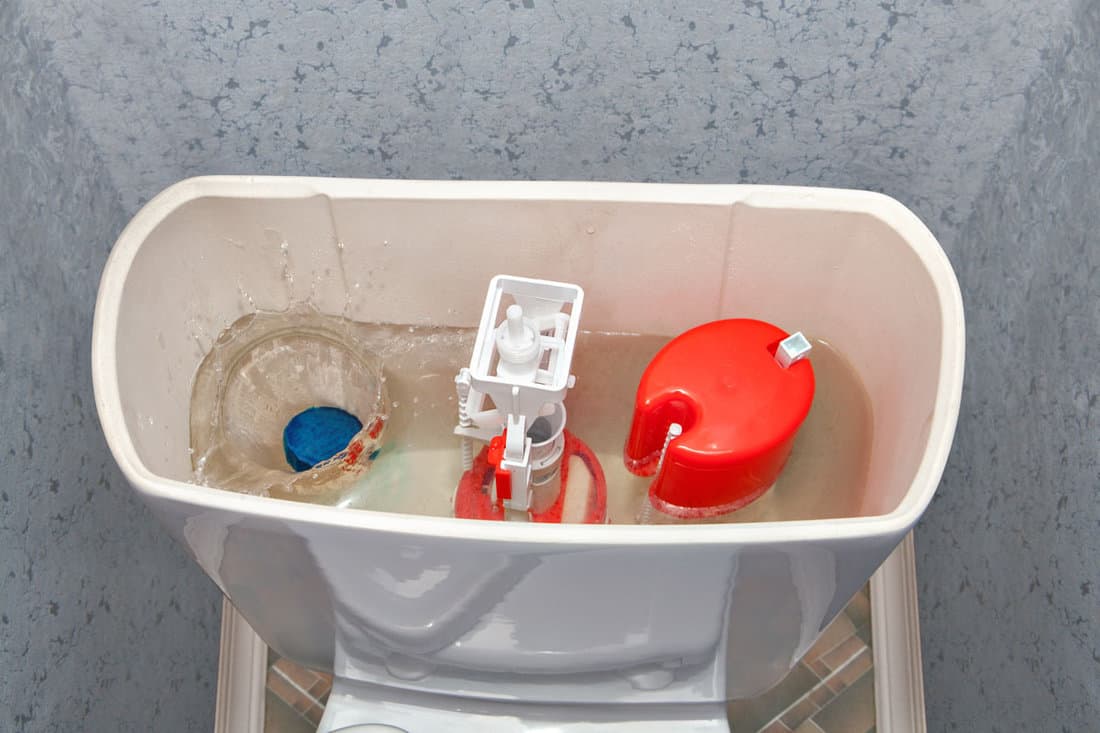 Blue cleaning water-soluble tablet falls into the water drain the toilet tank