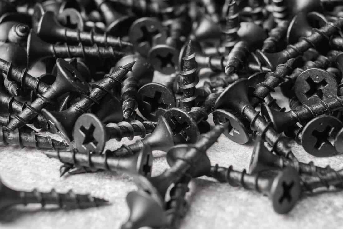 Building hardware background. Pile of self tapping black screws. Working tools close up. Selective focus