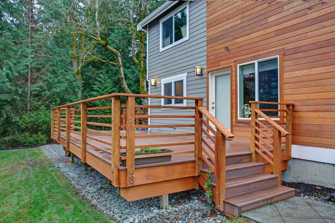 Charming newly renovated home exterior with mixed siding, Charming newly renovated home exterior, natural wood siding and grey siding create a beautiful curb appeal. Detail view of a nice walk out deck with wooden handrails.