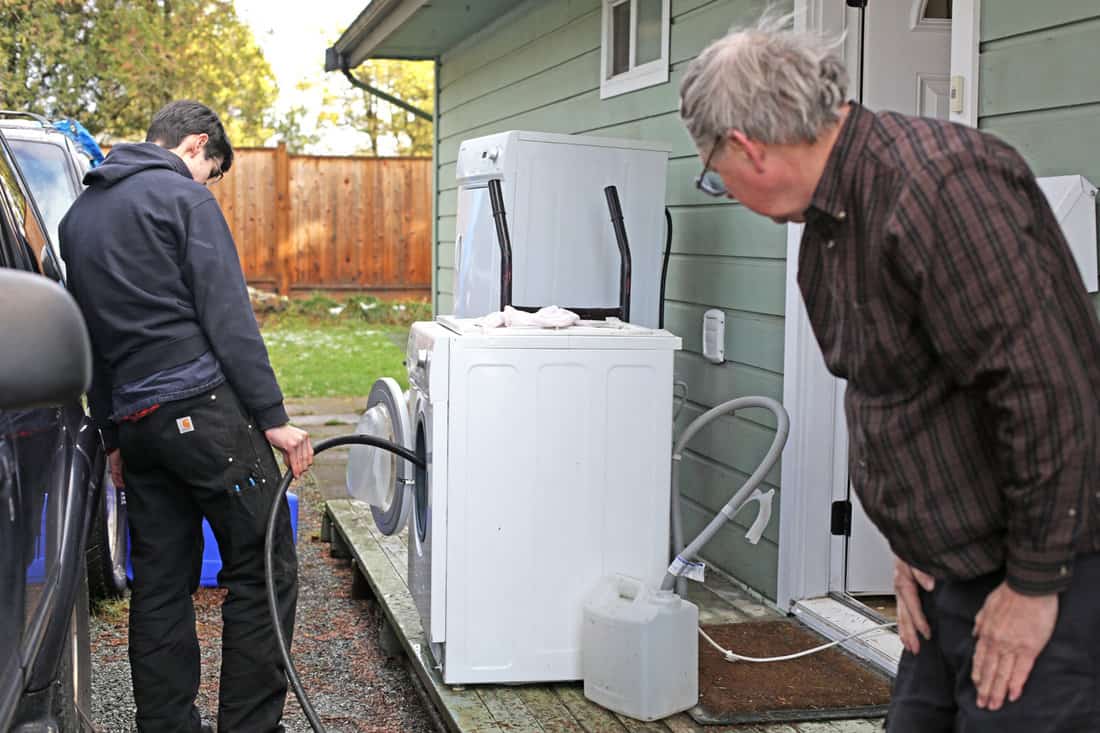Canadian father and son check water drainage on old washing machine outside their house in winter. DIY project.