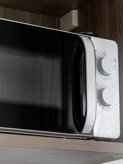 Close-Up White microwave on a wooden shelf in kitchen, Can You Put A Countertop Microwave In A Cabinet [And How To Install It]?