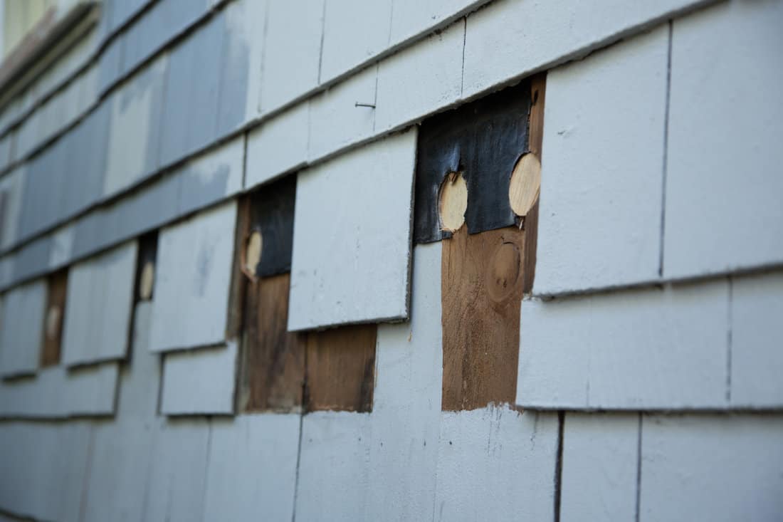 Close up of exterior suburb house siding repair of missing blue wood shingles under construction remodeling