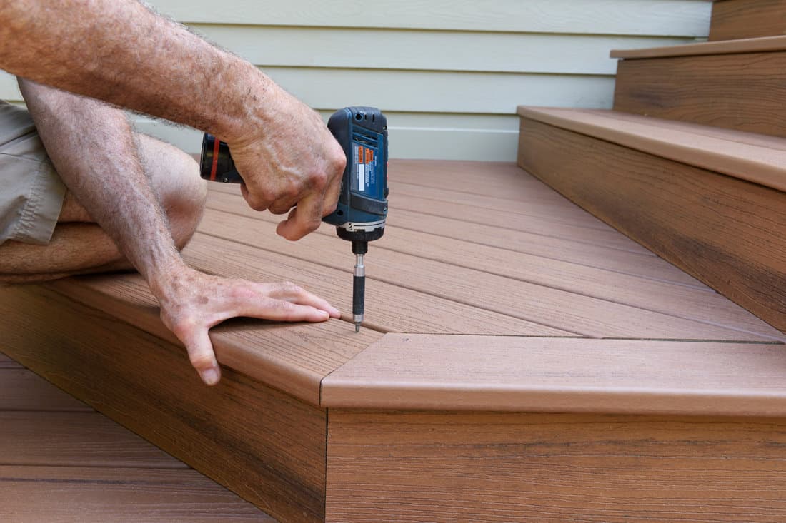 Close-up of worker using drill to install new porch decking, Worker Installing Composite Wood Decking 