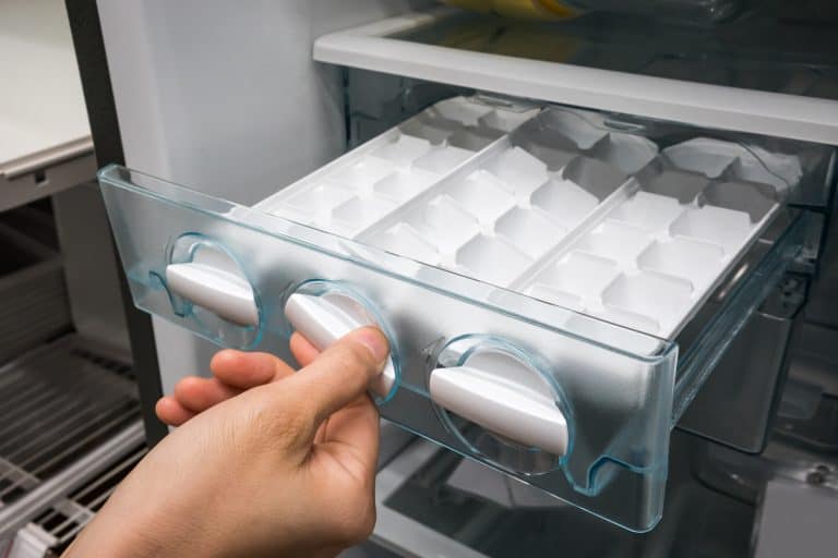 Closed up woman hand twisting for ice from the ice maker in new refrigerator - My Samsung Ice Maker Reset Is Not Working - What To Do