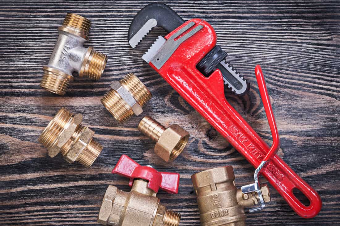 Collection of adjustable pipe wrench brass fittings water valve on wood board plumbing concept.