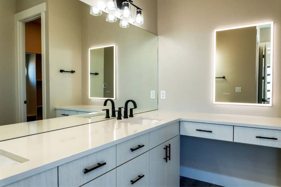 Contemporary style well lit bathroom with sinks, cabinets, and lighted vanity mirror