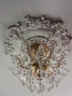 Crystal chandelier with a gold fixture and a white molded ceiling medallion on a white ceiling - How Wide Should A Ceiling Medallion Be