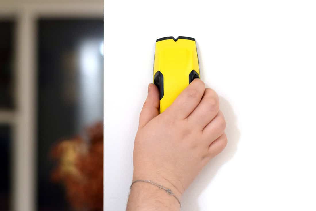 Female hand using stud finder to search apartment wall for studs and live wires