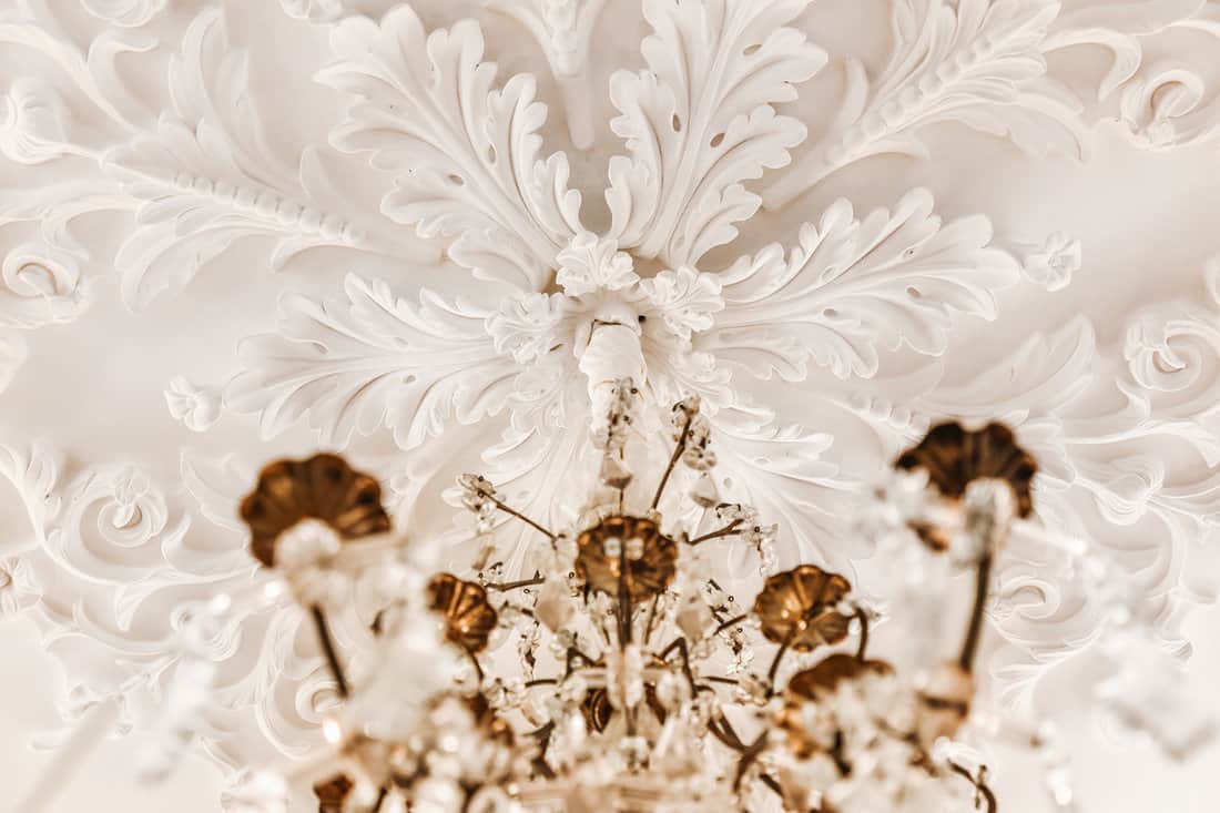 From below classic plaster floral ornament of medallion decorating ceiling above elegant chandelier at home