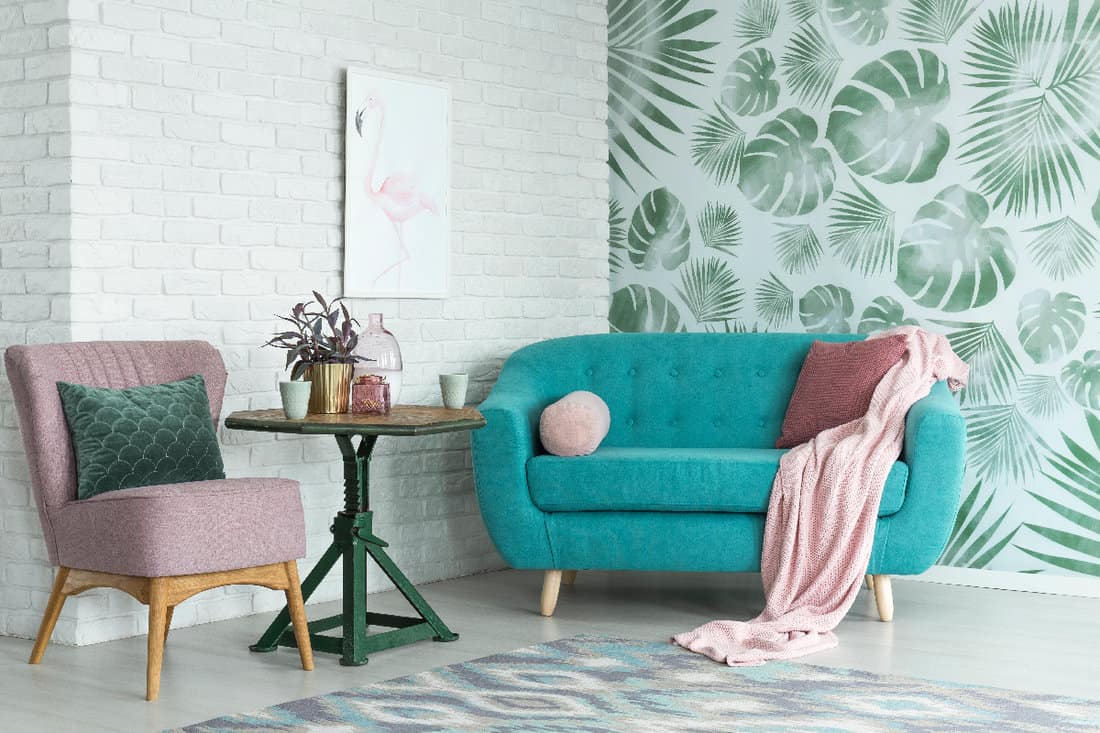 Green table with plant between pink chair and blue sofa in floral living room with wallpaper