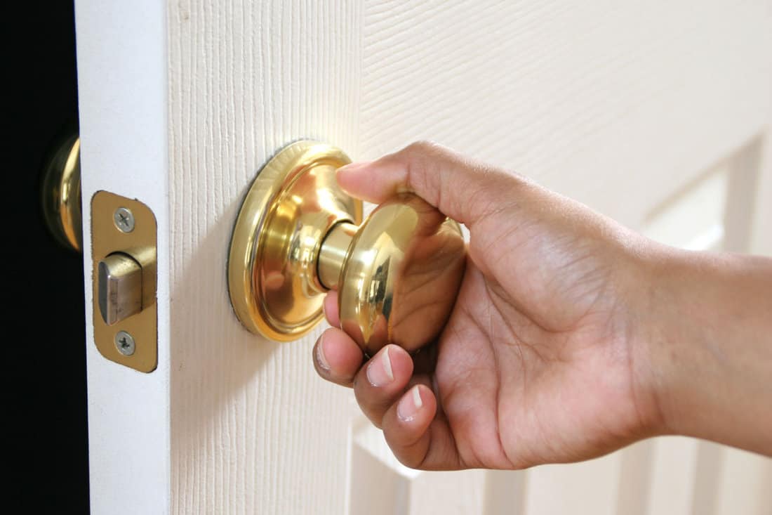 Hand holding a door knob opening a white door