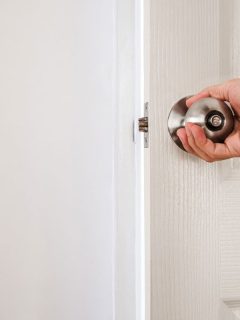Hand holding door knob, white door and wall, How To Install Portable Door Lock [Step By Step Guide]