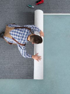 High Angle View Of Young Male Worker In Overalls Rolling Carpet On Floor At Home